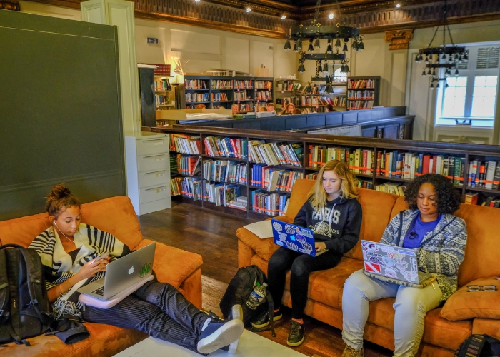 three students studying on laptops and sitting on couches in the MUDEC library
