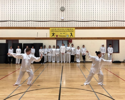 two students perform tai chi for the judges. They stand with their hands in front of them as they do their routine. 