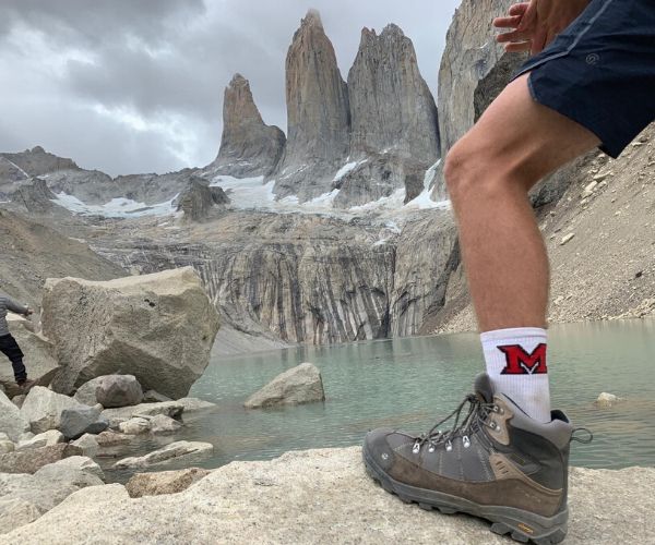 Miami student hiking, Miami sock in front of mountain and water