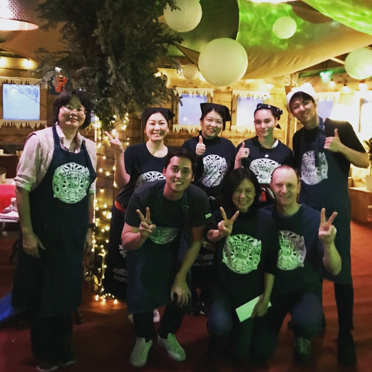 A smiling group of people wearing branded shirts and aprons at Manzoku