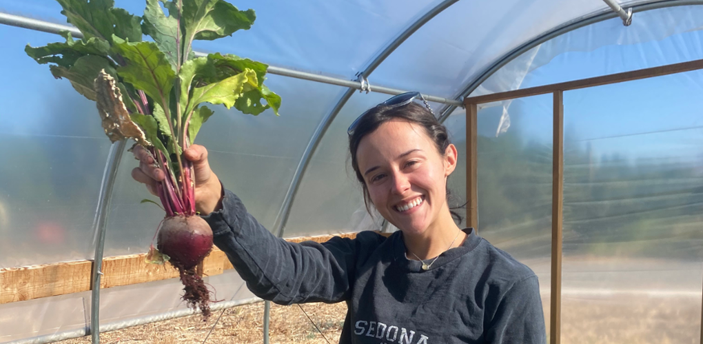 Grace smiles as she lifts a rutabaga overhead as she stands in a greenhouse