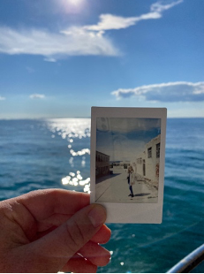 A hand holds up Goli Otok prison photo against the water