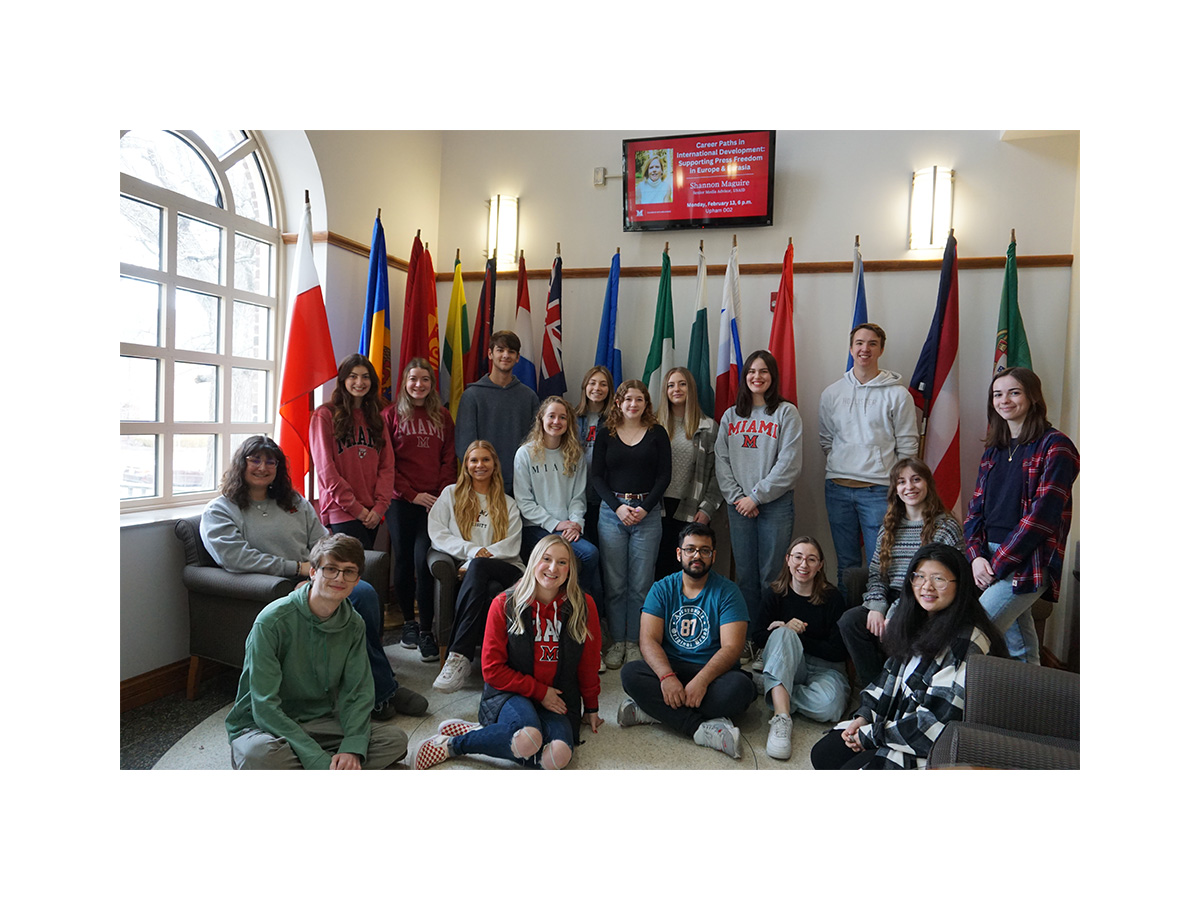 With international flags in the background, CCA cohort poses for a group picture in the lobby of MacMillan Hall