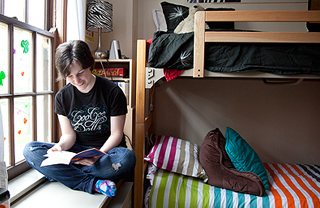Student sits in a residence hall room reading a book by the window.