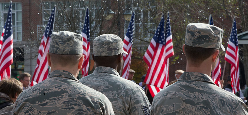 Members of the military stand facing American flags with their backs to the camera