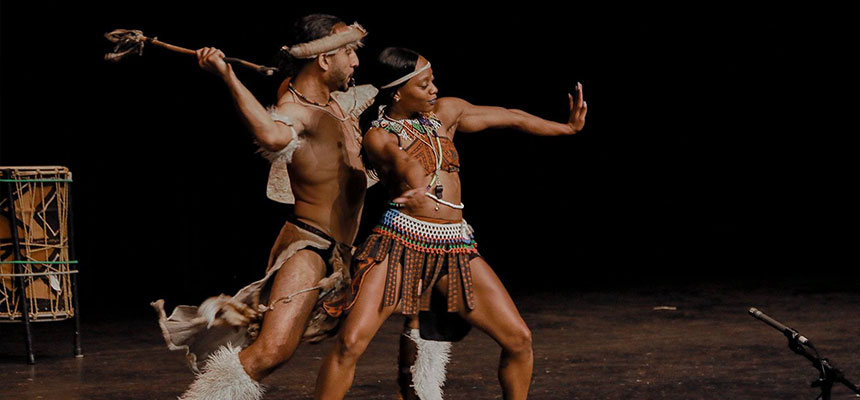Dancers on stage in traditional African attire at Dave Finkelman Auditorium.