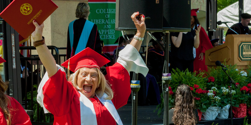 A TRIO grad with her hands up in the smiling after receiving her diploma.