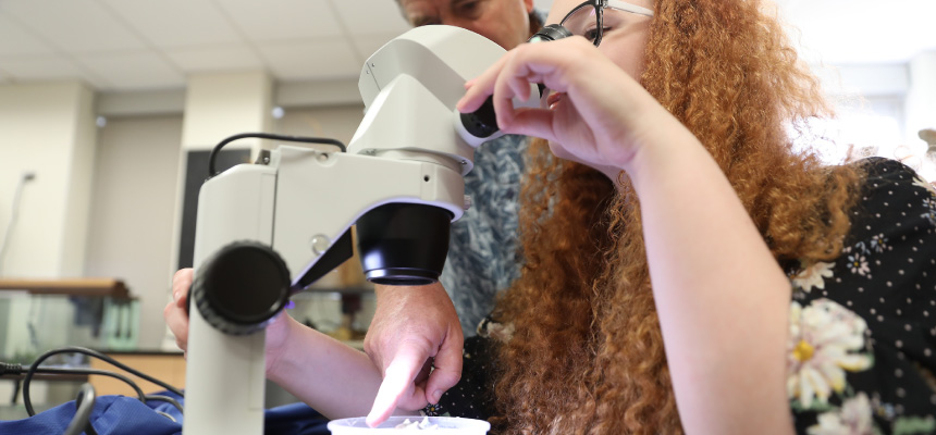 Professor Dave Berg showing a student a organism under a microscope.