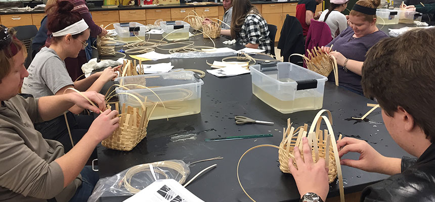 Students sitting at their desks working on weaving baskets.