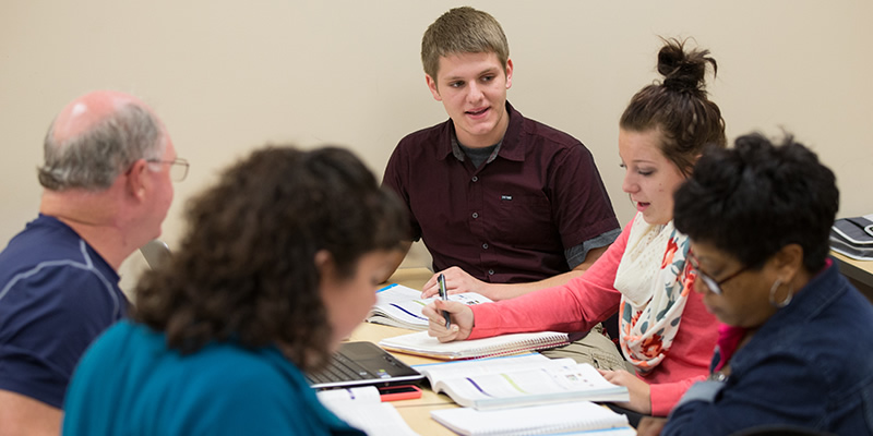 Students in an accounting course sitting at a table talking to one another.