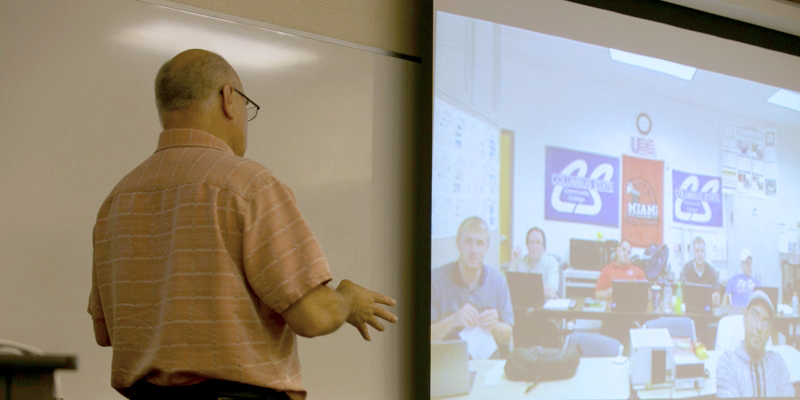 A professor teaching a course with a distance Learning site on the screen.