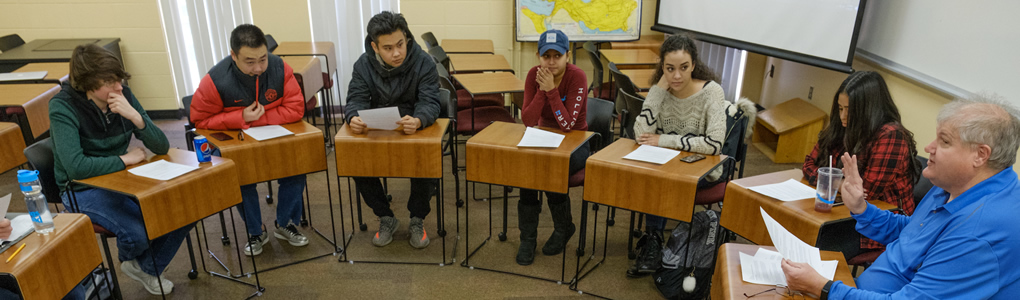 Professor Bob Weber sitting a desk in a circle with the students during class.
