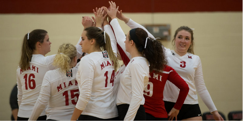 The volleyball team in a huddle with their hands in the air