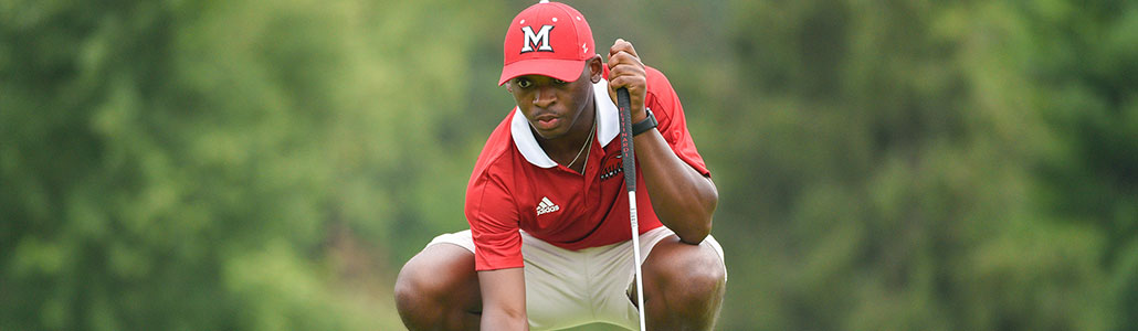 Hamilton golfer squatting on the green with his putter in his left hand.