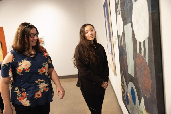 2 students looking at art on the wall of an art exhibit.