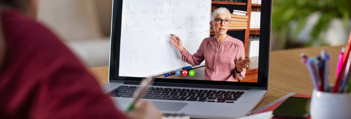 Person working on laptop and on the laptop screen you can see someone teaching in front of a white board