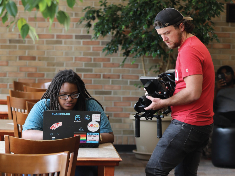 Videographer with a student while they work on their laptop