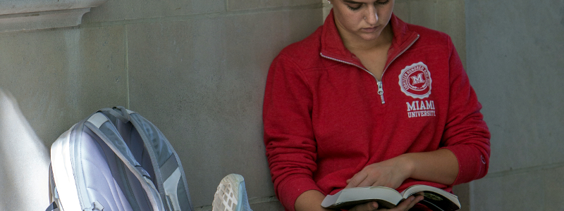 A student seated by a stone wall, reading