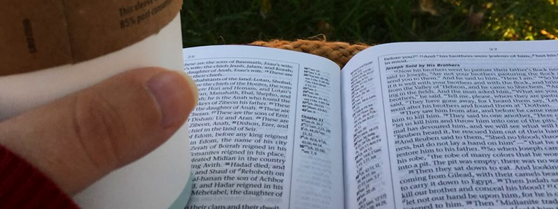 A POV shot of a person reading the Bible with a cup of coffee in hand