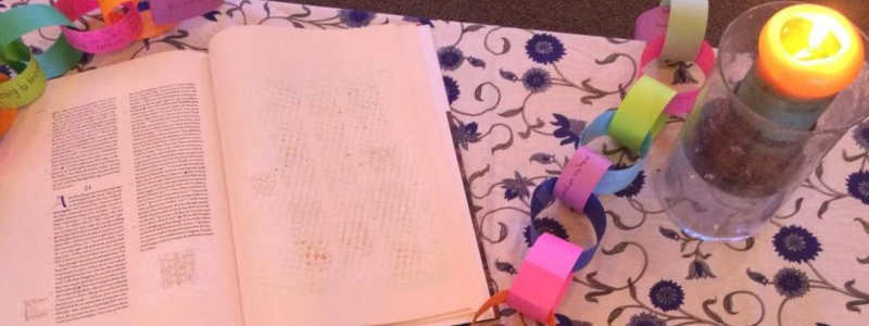 An open liturgical book, a paper chain, and a lit candle on a table