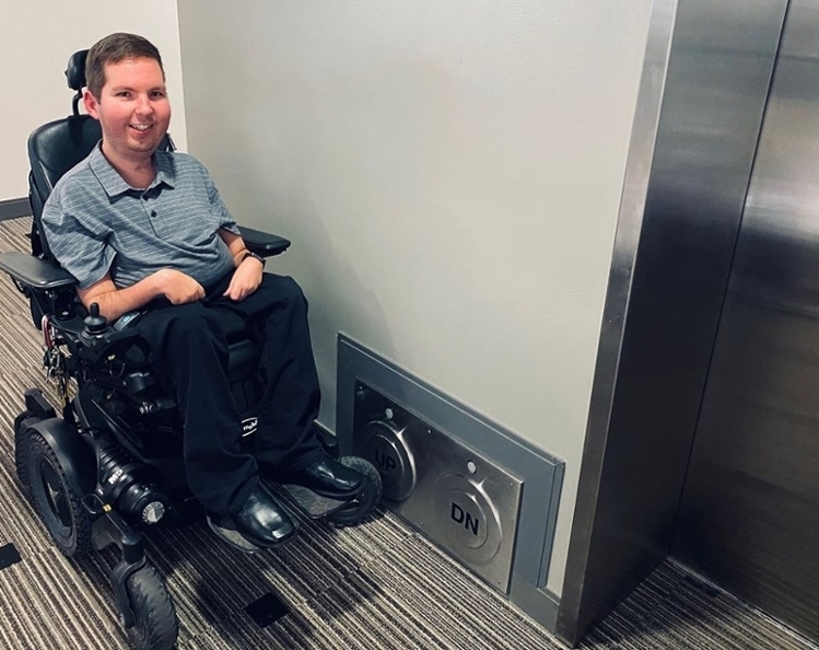 Wheelchair user Dan pushing the "UP" button with his wheelchair wheel calling the elevator to the current floor.