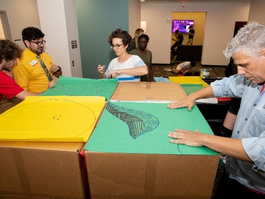 5 people gathered around four large cardboard boxes with colored construction paper on top