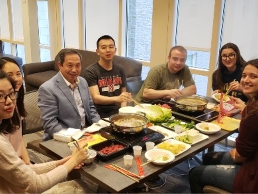 7 people seated at a table full of food, looking at the camera