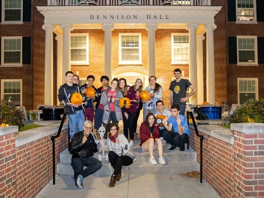 15 people posing on steps in front of Dennison Hall, many holding carved pumpkins