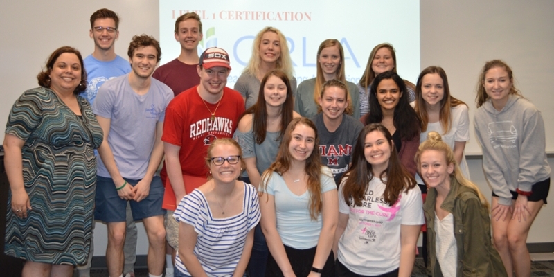 About 15 students posing and smiling in front of a projector screen