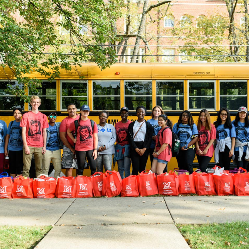 Group of students with hurricane relief supplies lined up in front of a yellow school bus