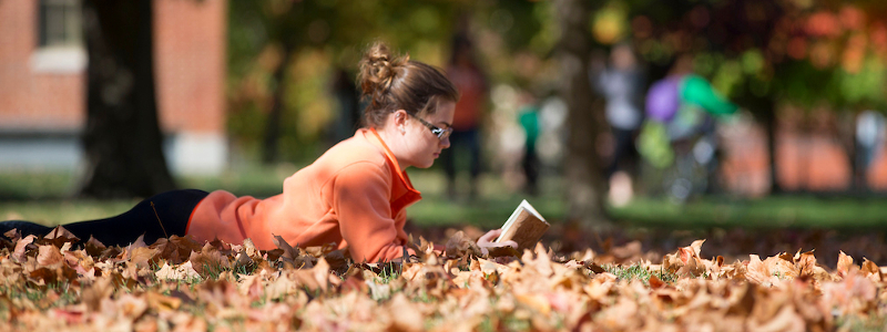 A student lying among autumn leaves, reading