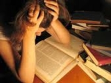 Student holding head, stressed, over an open book