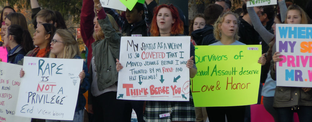 Several women engaged in protest holding signs that read, broadly, Rape is not a privilege, my status as a victim is so coveted taht I moved schools because I was taunted by my rapist and his friends. Survivors of sexual assault deserve love and honor.