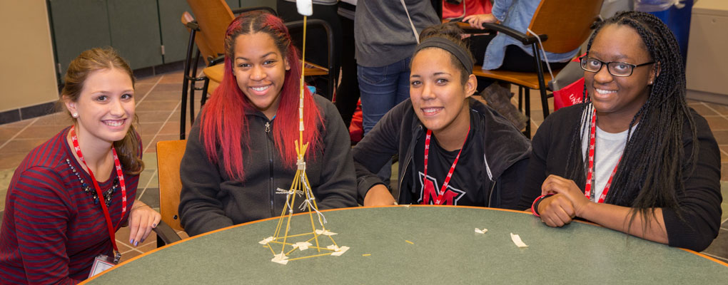 Four female students pose with a structure made out of dry spaghetti noodles and string