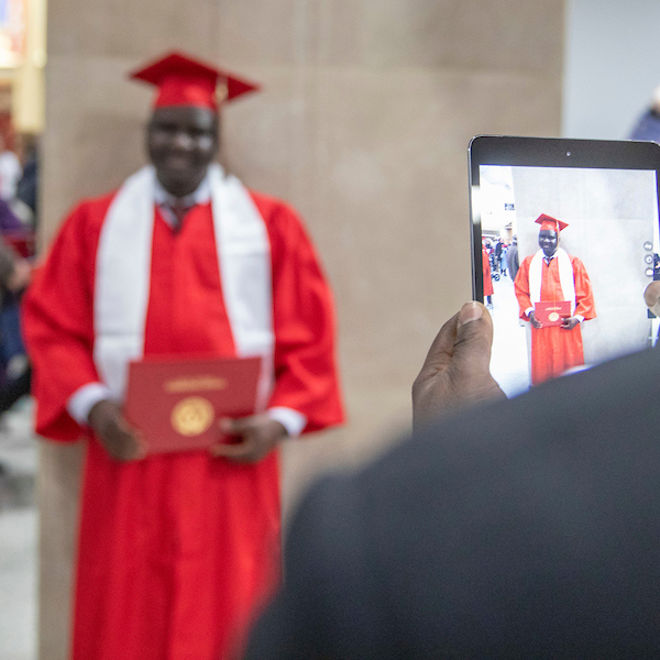 A black parent takes a photo of his graduating student with his phone.