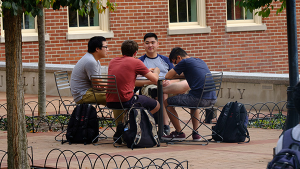  Four students sitting outside Armstrong Center at a cafe table discussing a group project.