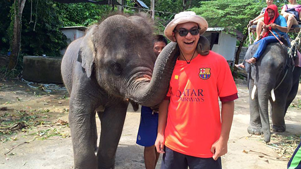  A student in another country with a baby elephant.  Elephant has trunk draped over student's neck.