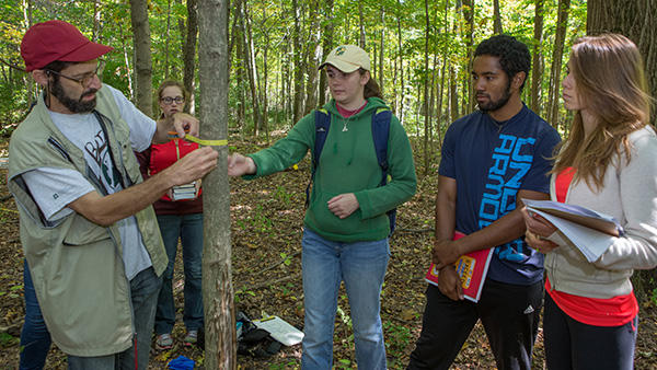  Instructor and several students measuring diameter of small tree in the forest. 