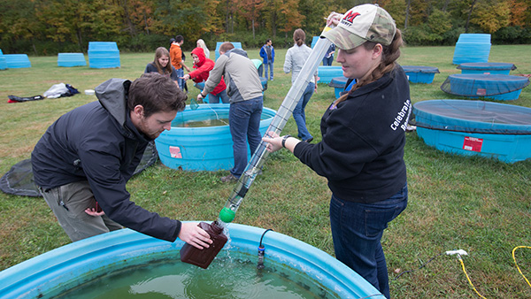  Two students using a large tube to draw water from an artificial test pool.
