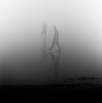 Two human figures walking in the fog