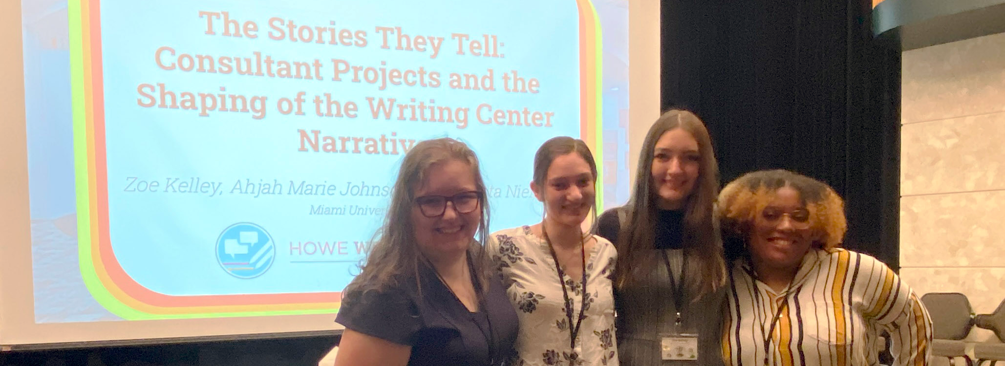 HWC Graduate Assistant Director and consultants Destiny Brugman, Christa Niemann, Zoe Kelley, and Ahjah Johnson, in front of a screen at the East Central Writing Centers Association Conference that reads "The Stories They Tell: Consultant Projects and the Shaping of the Writing Center Narriative
