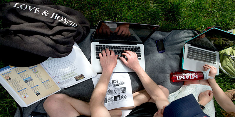 Hands poised above a laptop on the ground outside, viewed from above