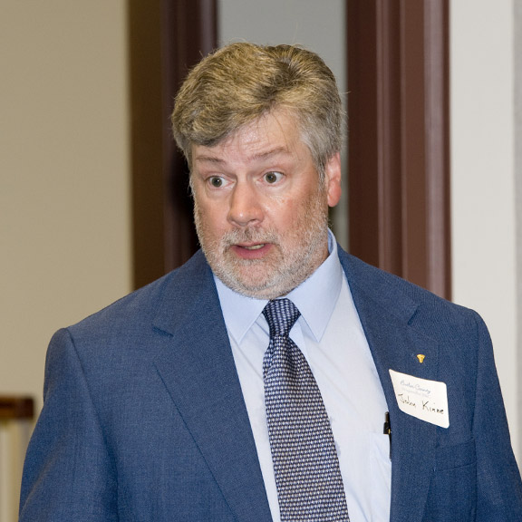 John Kinne in a blue suit, wearing a name tag and talking