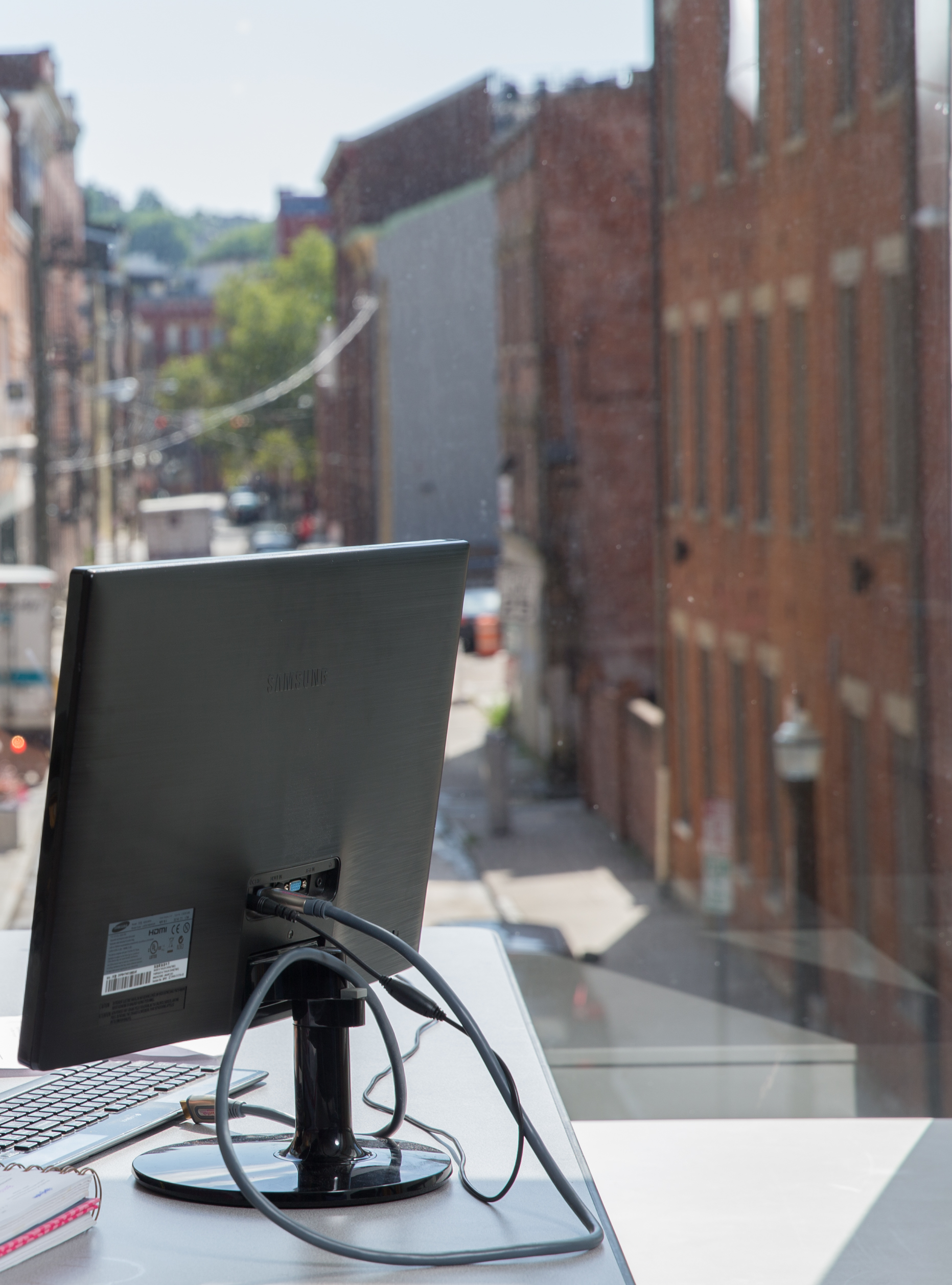 Computer monitor sitting on a desk with a view of downtown Cincinnati in the the background through a window