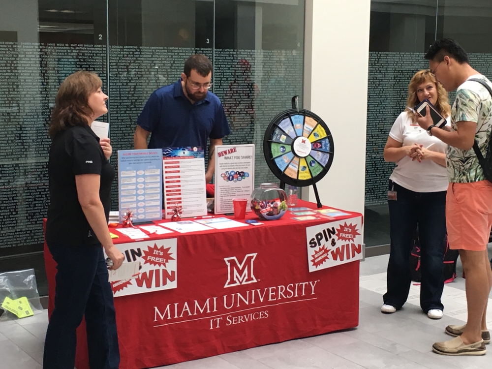 IT Services security awareness table with prize wheel and Connie Johnson, Lisa Raatz and Chris Linebrink assisting a student
