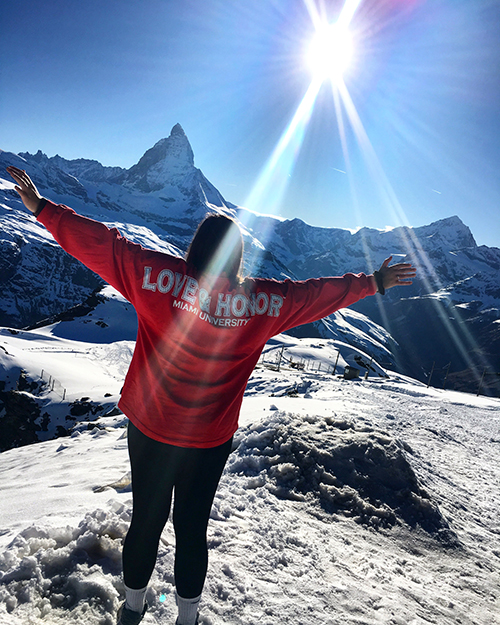 Person standing on a snowy mountaintop. The back of their red sweatshirt says Love and Honor in white lettors