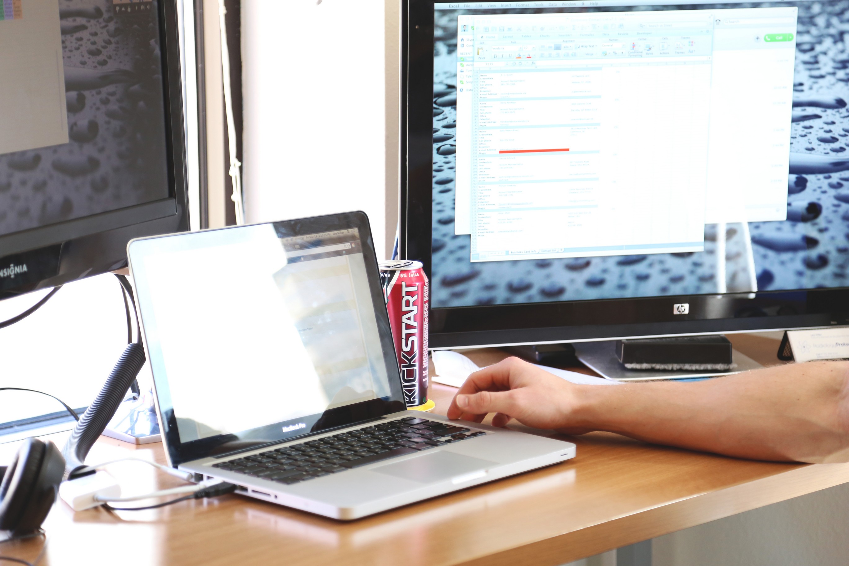 A home workstation with a laptop, monitor, and a man's arm sitting on a desk