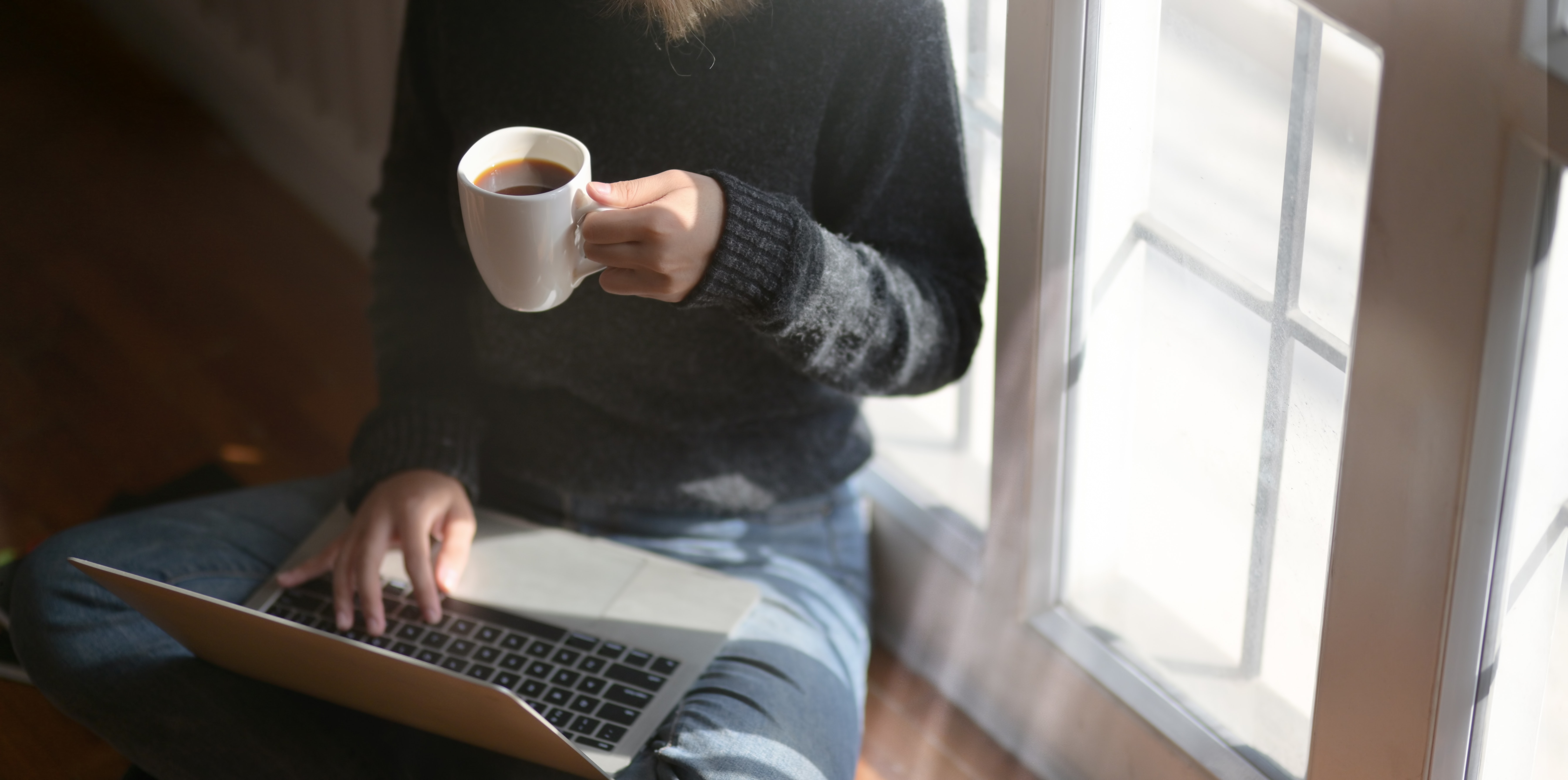 A female-presenting person with a cup of coffee sits with a computer in their lap