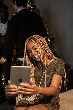 A young woman taking a photo of herself with an iPad, in front of a holiday tree