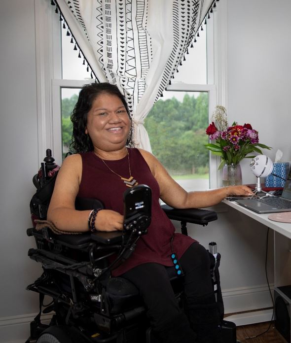 Liz Persaud smiles in her home office. She is a wheelchair user with dark hair